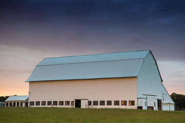 Obraz premium White barn at sunset in a green, grassy field under a sky with purple, yellow, and orange clouds - Willamette Valley, Oregon