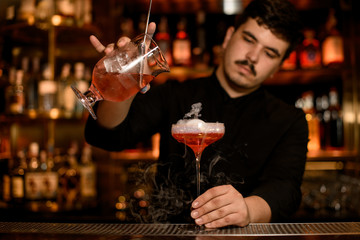 Bartender with strainer prepares an alcohol drink