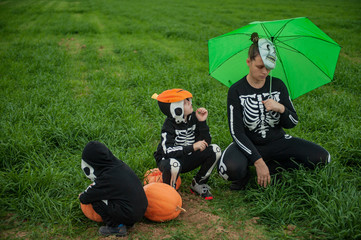 Girl mother with children in skeleton bone on green field with umbrella with pumpkins on eve of  holiday Halloween