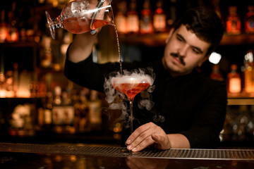 Bartender with strainer preparing an alcohol cocktail