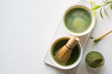 Ceremony traditional green matcha tea in bowl and bamboo whisk on white concrete table. Top view....