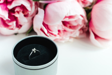 Obraz na płótnie Canvas Diamond ring in a box, pink peonies flowers on white background, copy space