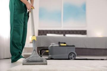 Professional janitor removing dirt from carpet with vacuum cleaner in bedroom, closeup. Space for...