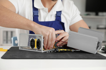 Male technician repairing power supply unit at table indoors, closeup