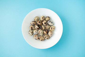 Raw quail eggs in white plate on blue background. Easter.