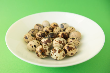 Raw quail eggs in white plate on green background. Easter.