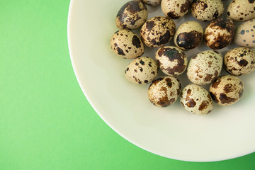Raw quail eggs in white plate on green background. Easter.