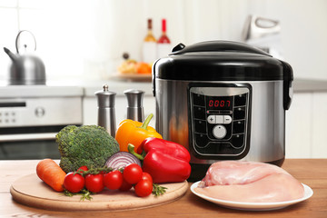 Modern multi cooker and products on wooden table in kitchen. Space for text