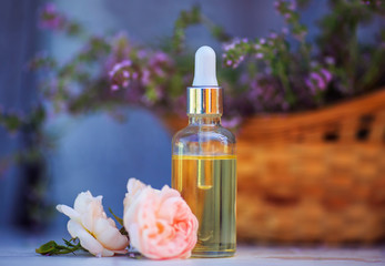 bottle with cosmetic rose oil and a pipette stands on a wooden table in delicate lavender colors outside