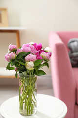 Vase with bouquet of beautiful peonies on table in room