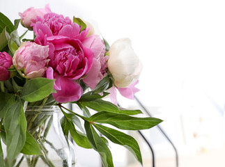 Vase with bouquet of beautiful peonies near white wall, space for text