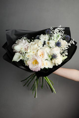 stylish bouquet of flowers in black dark paper packaging, white light lush flowers