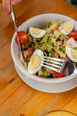 Traditional american cobb salad with chopped avocado, tomatoes, hard boiled egg, roasted chicken and greens for a healthy lunch, served on wooden table with soft light