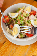 Traditional american cobb salad with chopped avocado, tomatoes, hard boiled egg, roasted chicken and greens for a healthy lunch, served on wooden table with soft light