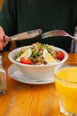 Woman is eating traditional american cobb salad with chopped avocado, tomatoes, hard boiled egg, roasted chicken and greens for a healthy lunch