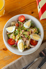 Top view of traditional american cobb salad with chopped avocado, tomatoes, hard boiled egg, roasted chicken and greens for a healthy lunch, served on wooden table with soft light