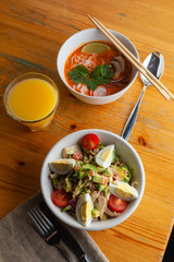 Healthy lunch with tomato noodle soup and traditional american cobb salad and orange juice, served on a wooden table in a restaurant with soft light