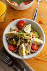 Traditional american cobb salad with chopped avocado, tomatoes, hard boiled egg, roasted chicken and greens for a healthy lunch, served on wooden table with soft light