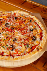 Close up of round pizza on thin dough with grilled chicken breast, bell pepper, champignons, cheese and ricotta, served on wooden rustic table