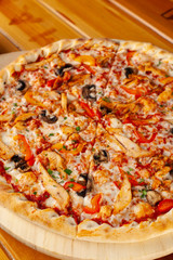 Close up of round pizza on thin dough with grilled chicken breast, bell pepper, champignons, cheese and ricotta, served on wooden rustic table