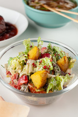 Close up of nutritious rustic-style salad with mixed greens, vegetables, roasted potato wedges and red onion, served with other meals on a background