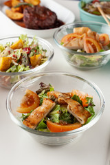 Close up of nutritious rustic-style salad with mixed greens, vegetables, roasted potato wedges and red onion, served with other meals on a background