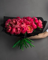 a large lush bouquet of red peonies and buds in black wrapping paper, a stylish bouquet of flowers