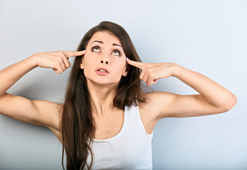 Young beauiful girl showing finger gun gesture, shooting herself and looking up on blue background. Closeup