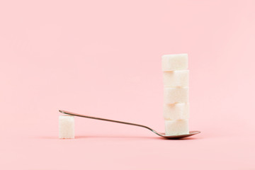 Sugar cubes in a spoon on pink background