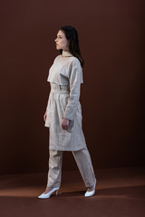 stylish model in trendy wear and white shoes walking on brown background