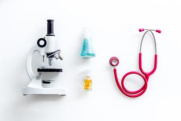 Do medical research with microscope, stethoscope, test-tubes in lab on white background top view