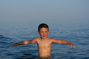 A boy of three years is swimming in the sea at sunset with his brother.