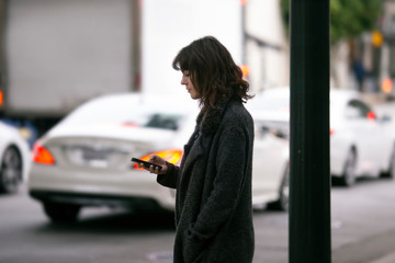 Female pedestrian waiting for a rideshare.  She is sharing her gps location via cellphone app so...