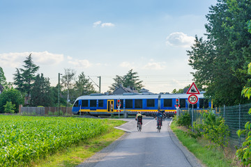 Outdoor sunny view of cyclists stop in front of level crossing railway barrier waiting for a train and green traffic light in small village countryside in Germany.