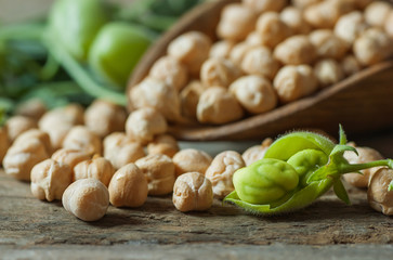 Uncooked dried chickpeas in wooden spoon with raw green chickpea pod plant on wooden table. Heap of...