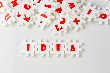 White puzzle jigsaws with alphabets building word IDEA at the center of other alphabets on white background, business idea, creativity or inspiration in work and problem solving