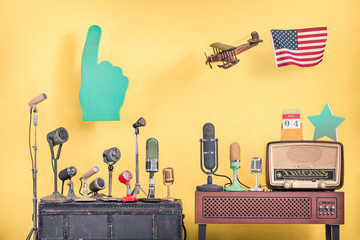 Retro microphones, flying wooden toy plane with USA flag, big pointing finger, old radio from 50s, 4th of July on desk calendar and award star front yellow background. Vintage style filtered photo