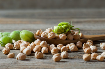 Uncooked dried chickpeas in wooden spoon with raw green chickpea pod plant on wooden table. Heap of...