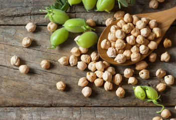 Uncooked dried chickpeas in wooden spoon with raw green chickpea pod plant on wooden table. Heap of legume chickpea background