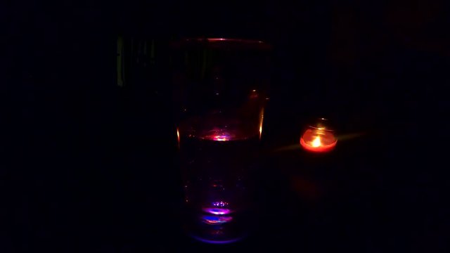 LOOPING - Champagne rotating on a LED panel in a dark restaurant setting with a red lit candle in the background.