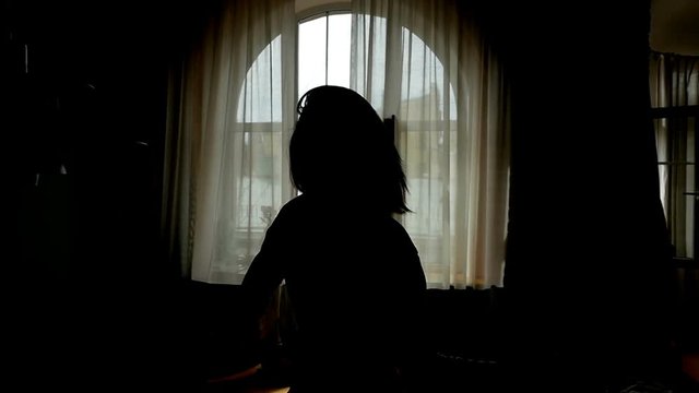 Rear view of young woman opening curtains on window at morning and go out to balcony. Silhouette of girl goes to window