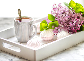 Tea is served on a wooden tray with marshmallows and a bouquet of lilacs. Close-up