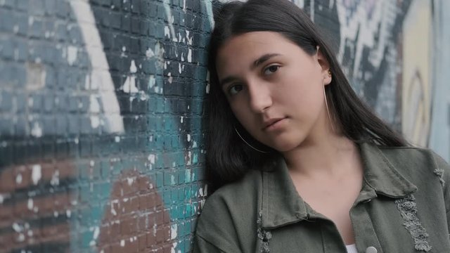 portrait of a young sad brunette hipster girl with brown eyes near a wall with graffiti