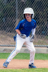 Youth baseball player in blue uniform and white helmet anticipating the right time to run.