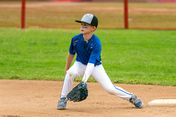 Youth baseball player in blue uniform covering second base and waiting for the ball in the infield during a game.