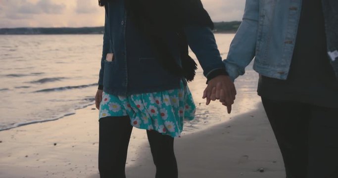 Two young women holding hands on the beach after sunset