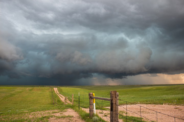 A dark storm looms on the horizon at the end of a dirt road in the countryside.