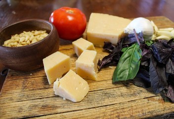 Ingredients for making home made pesto including parmesan cheese, fresh purple and green basil, garlic and pine nuts on wooden board