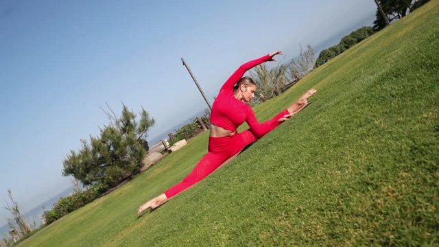 Young blonde woman in red latex costume is doing yoga exercises.