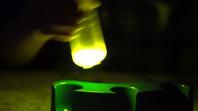 A lab tube glowing in the dark. A mix of phenyl oxalate ester and hydrogen peroxide causes a chemical reaction that illuminates the dark with a bright and colorful liquid substance.